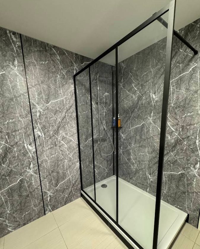 Douche fermée par une paroi coulissante noire, murs marbre gris