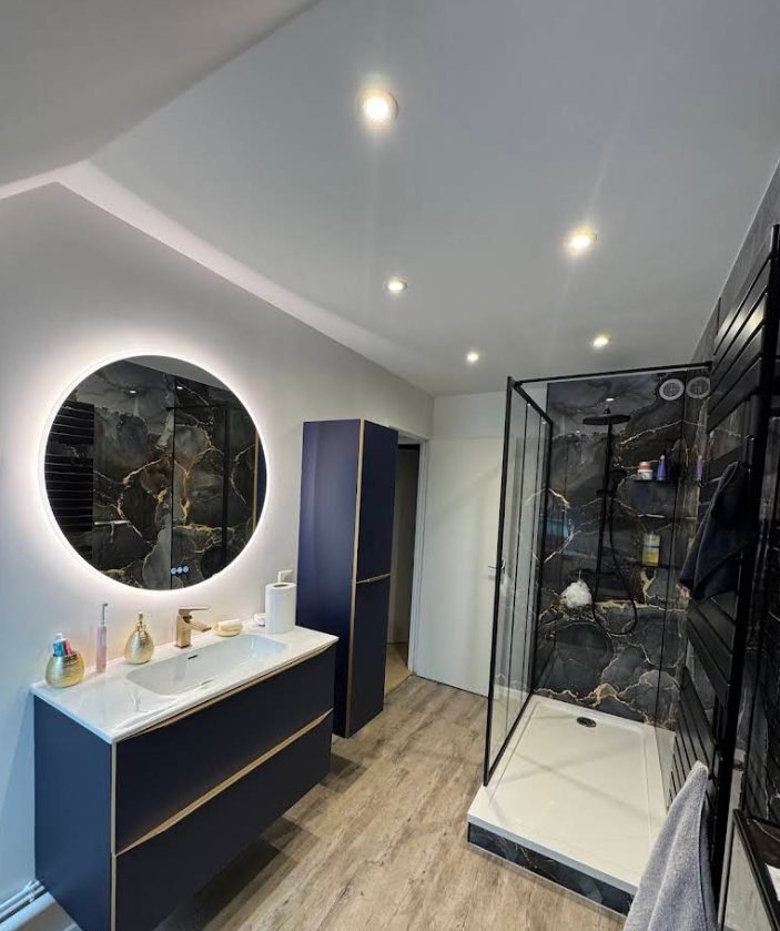 Salle d'eau sous combles : meuble suspendu bleu nuit, miroir rond rétroéclairé et douche à receveur extra-plat